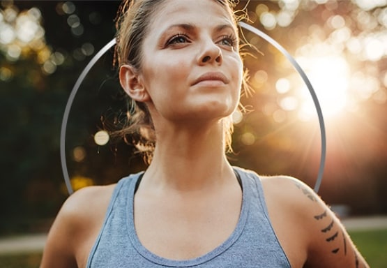 Active young woman wearing tank top, standing in empowered pose against a sunny backdrop